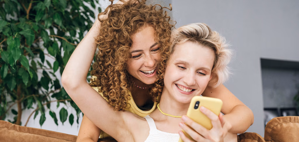 Two women laughing at a phone together on a couch