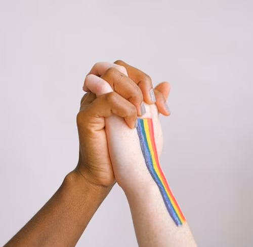 Two women holding hands, one with a rainbow painted on her arm
